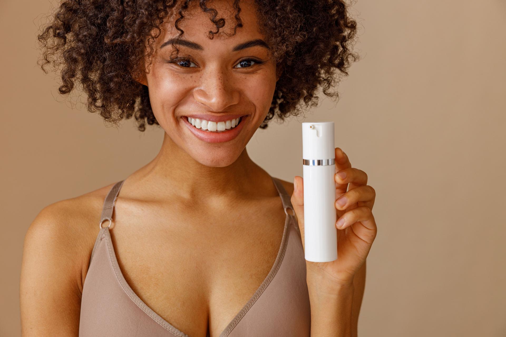 Young woman holding bottle with beauty product in studio