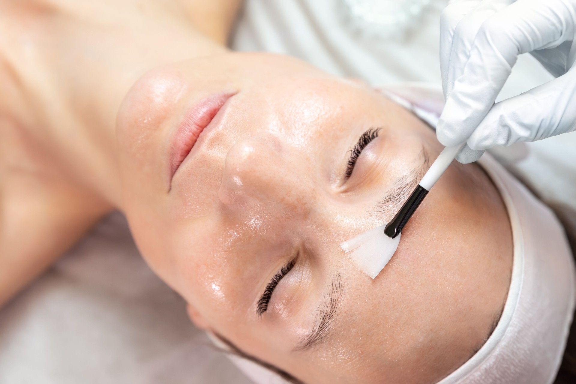 Close-up beautician doctor hand making anti-age procedure apply peeling acid young attractive female client at beauty clinic. Cosmetologist specialist doing skincare treatment. Health care therapy